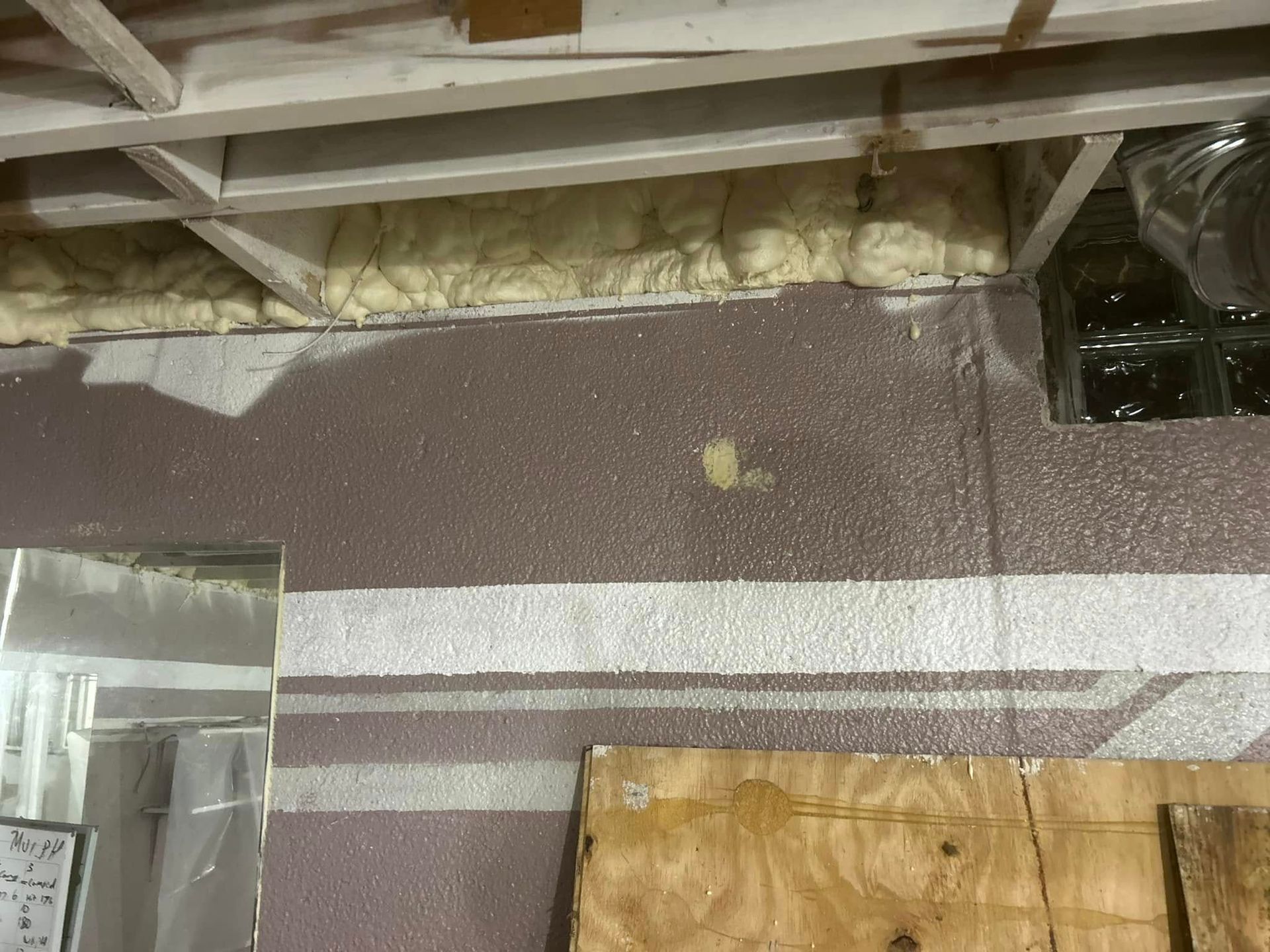 Basement wall with pink insulation, white stripe, and exposed ceiling beams.