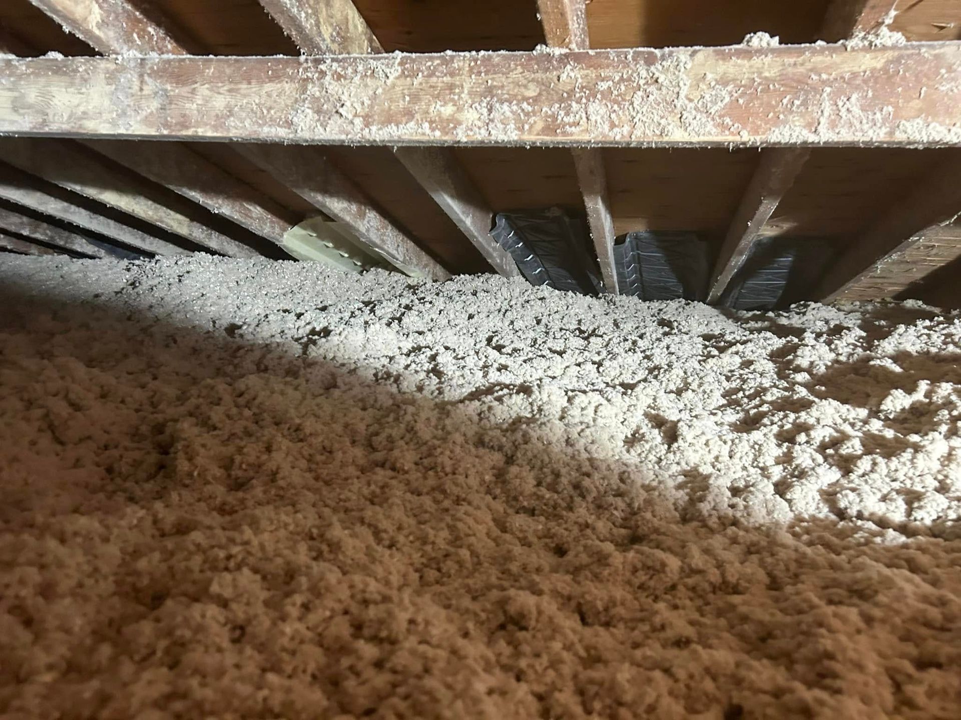 Attic filled with thick, light-colored insulation beneath wooden beams and a dark, unseen space.