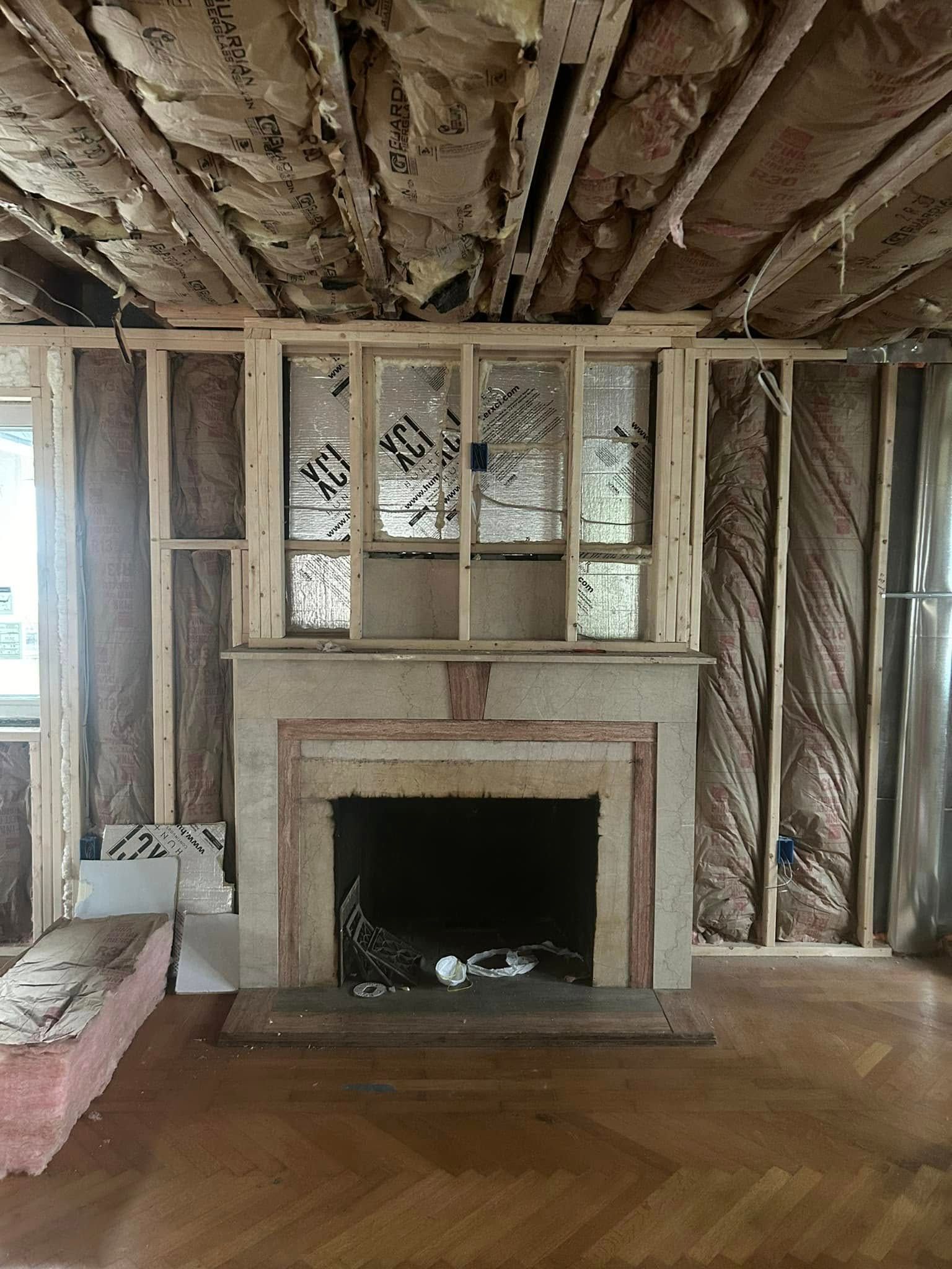 Fireplace framed in a room under construction; exposed studs, insulation, and unfinished ceiling.