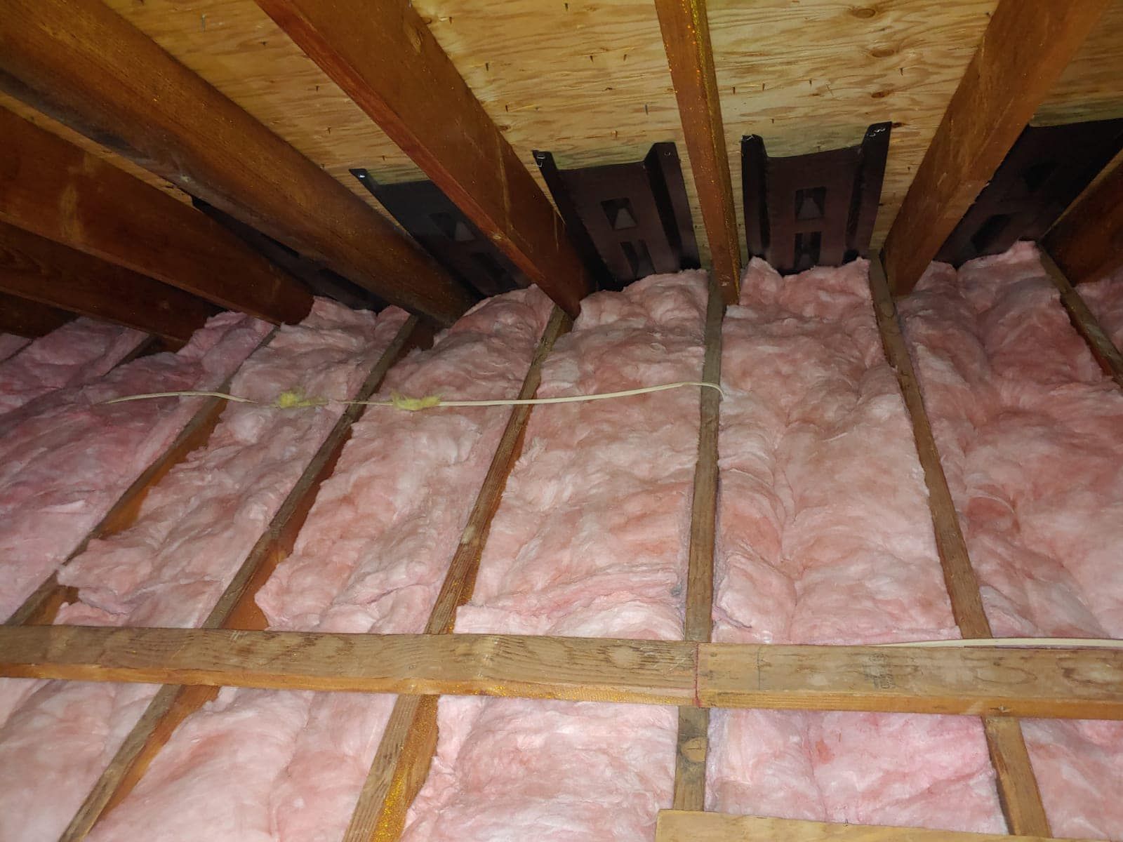 Pink insulation fills the space between wooden rafters in an attic.