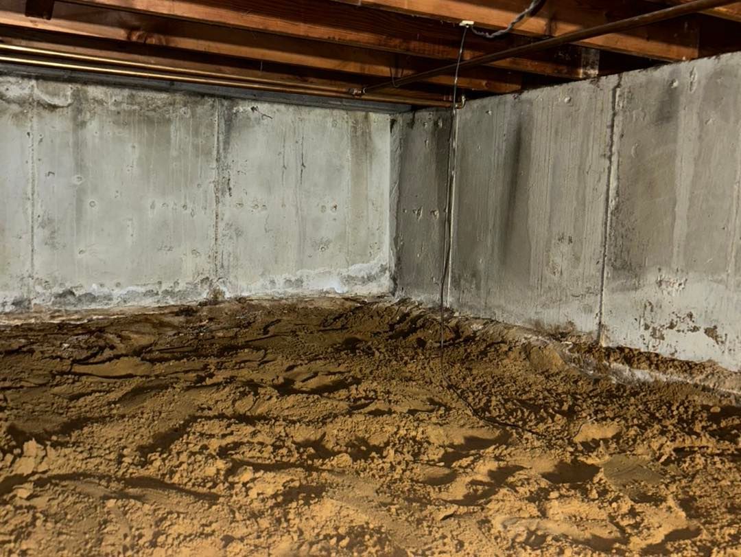 Dirt floor in a basement with concrete walls, a corner of the walls. Brown and gray tones.