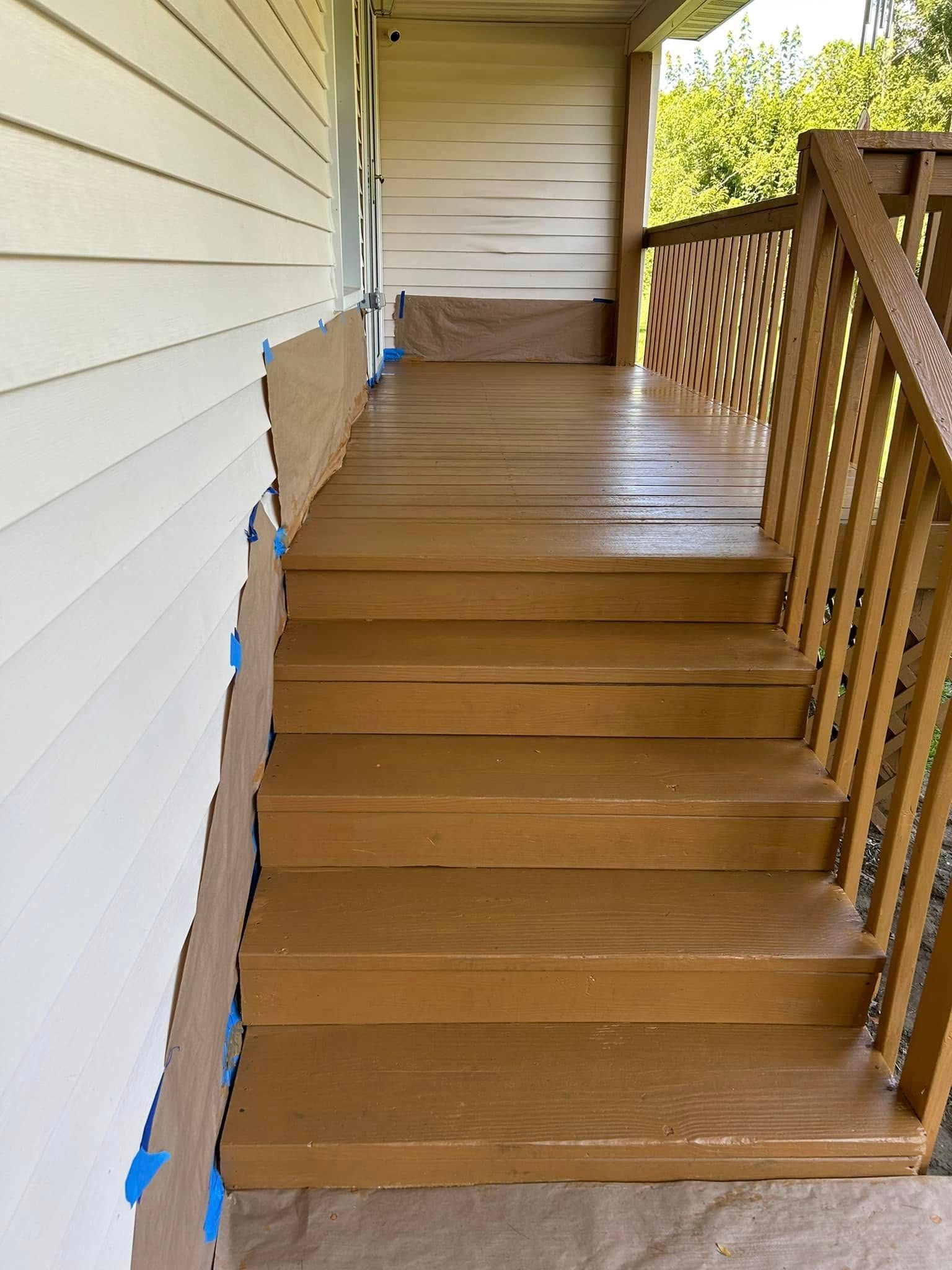 Brown painted wooden porch steps with railing, next to white house siding.