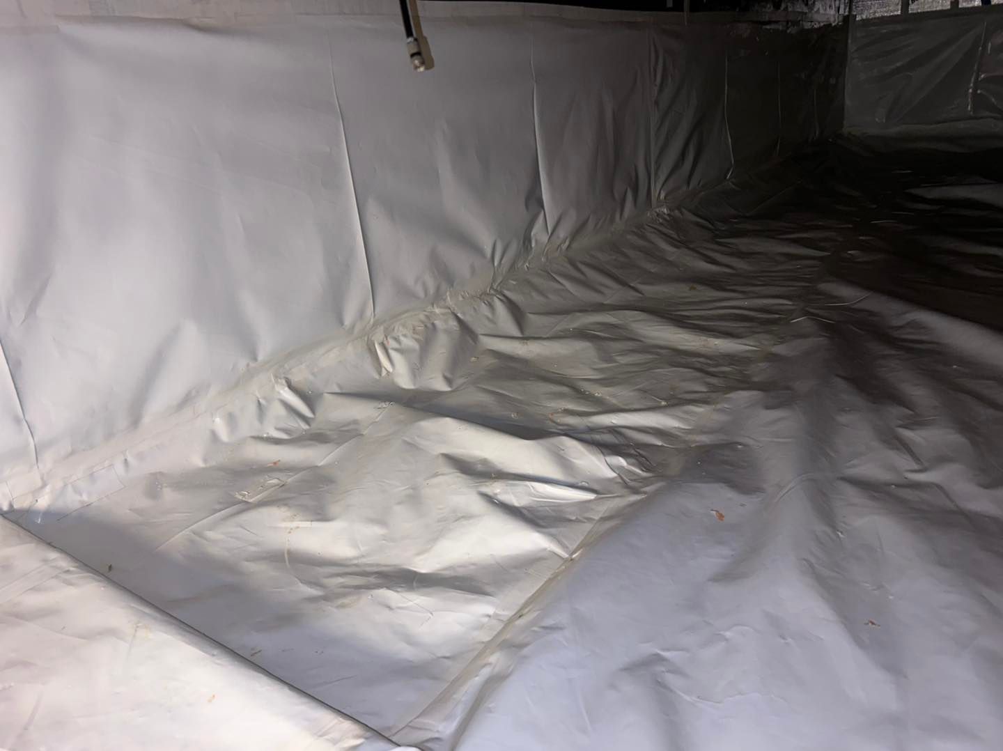 Crawl space with brick foundation, insulation, and a person inspecting with a flashlight.