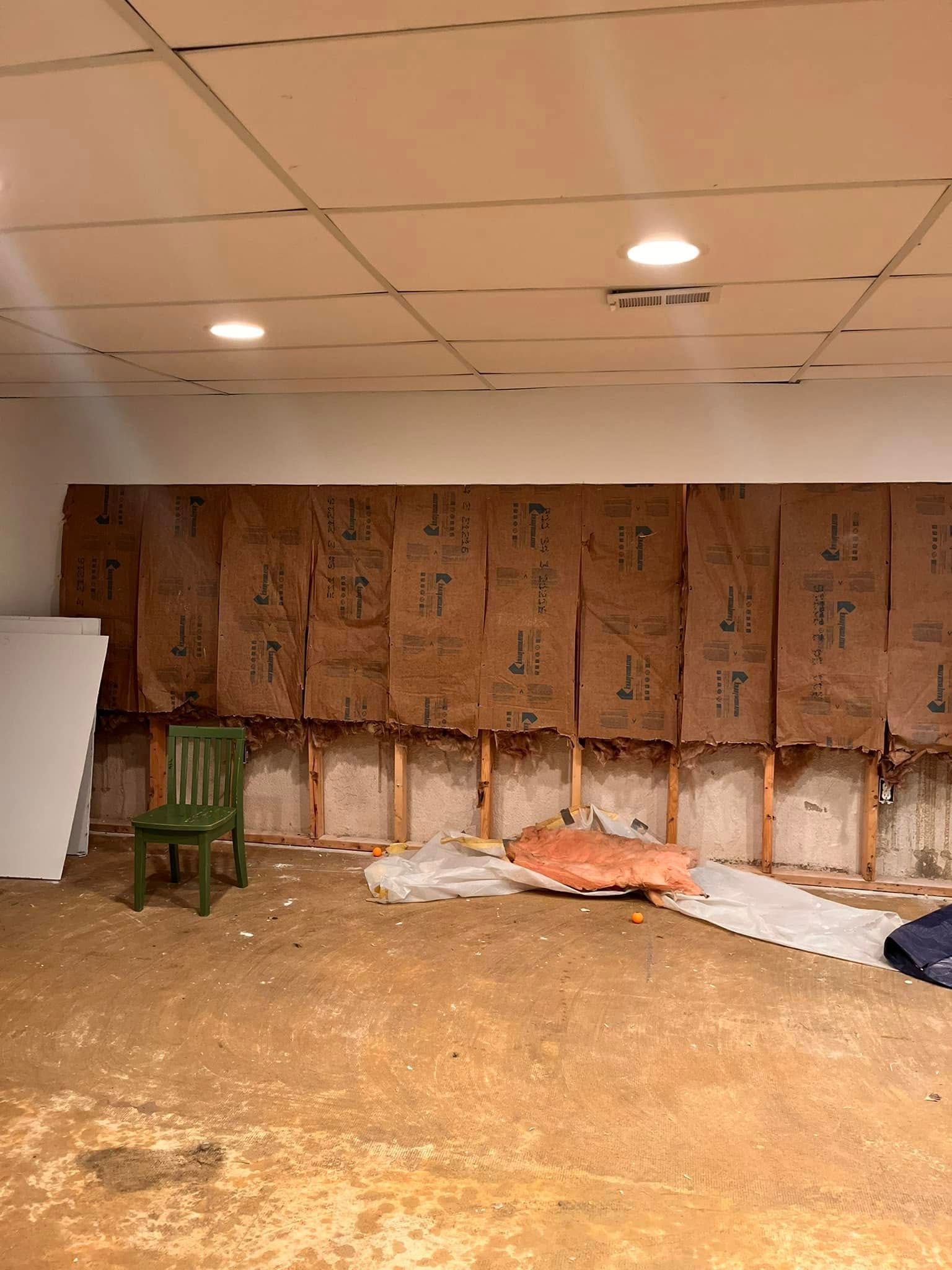 Basement wall with exposed framing, insulation, and a green chair. The floor is concrete.