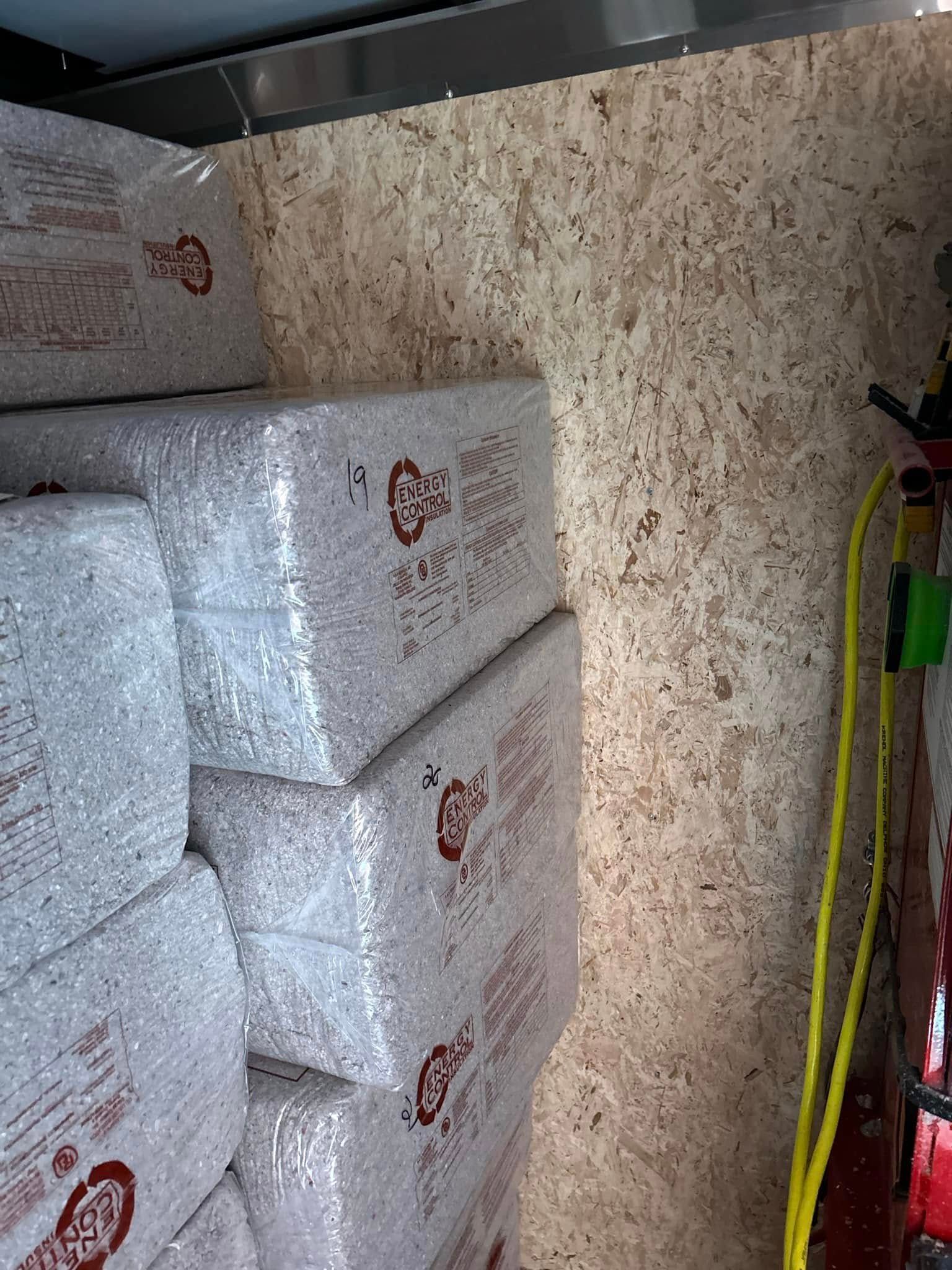 Piles of packaged goods inside a trailer. The side wall is particle board with a yellow air hose.