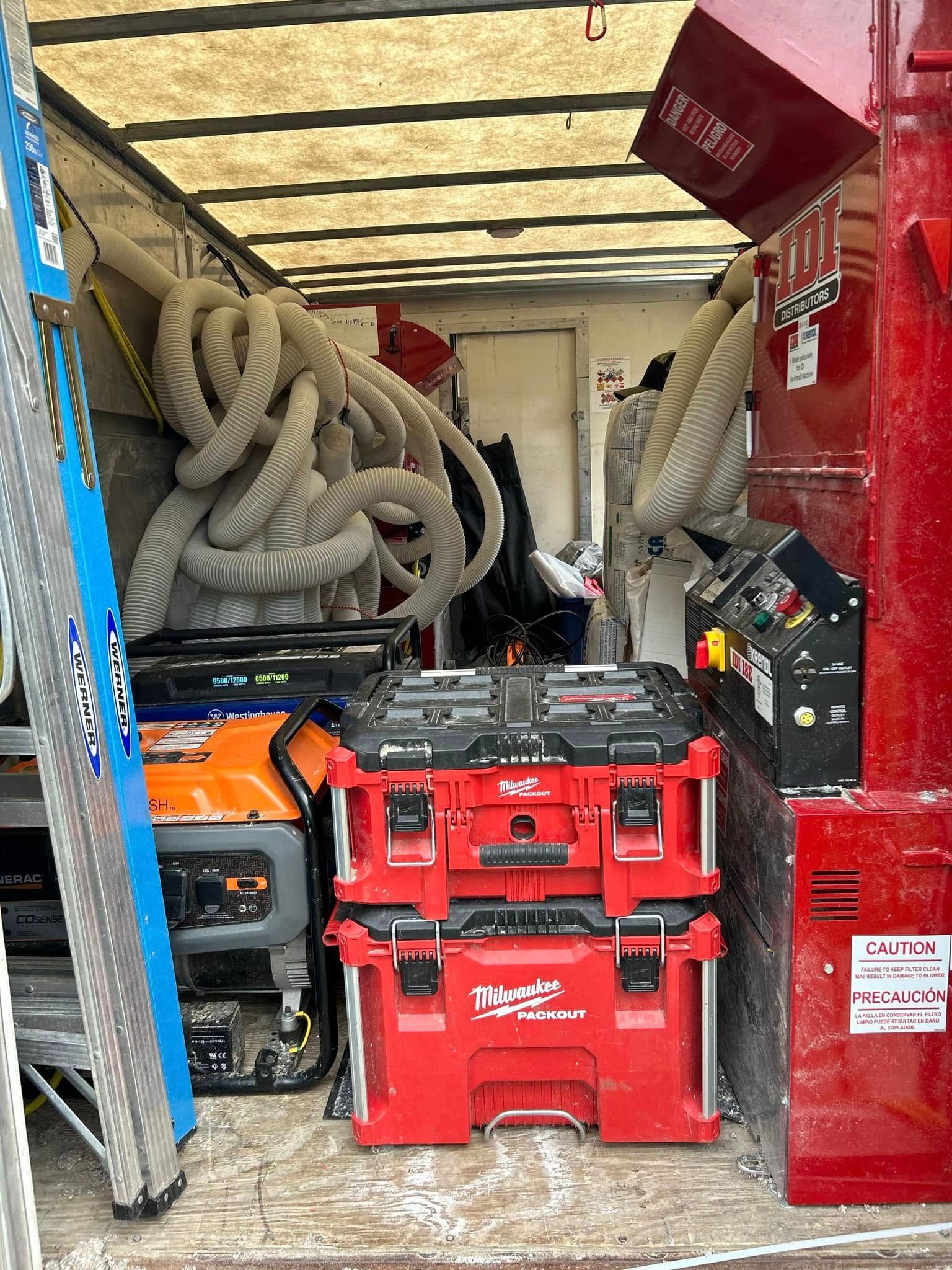 Interior of a cluttered truck with tools, equipment, hoses, and a stack of red Milwaukee toolboxes.