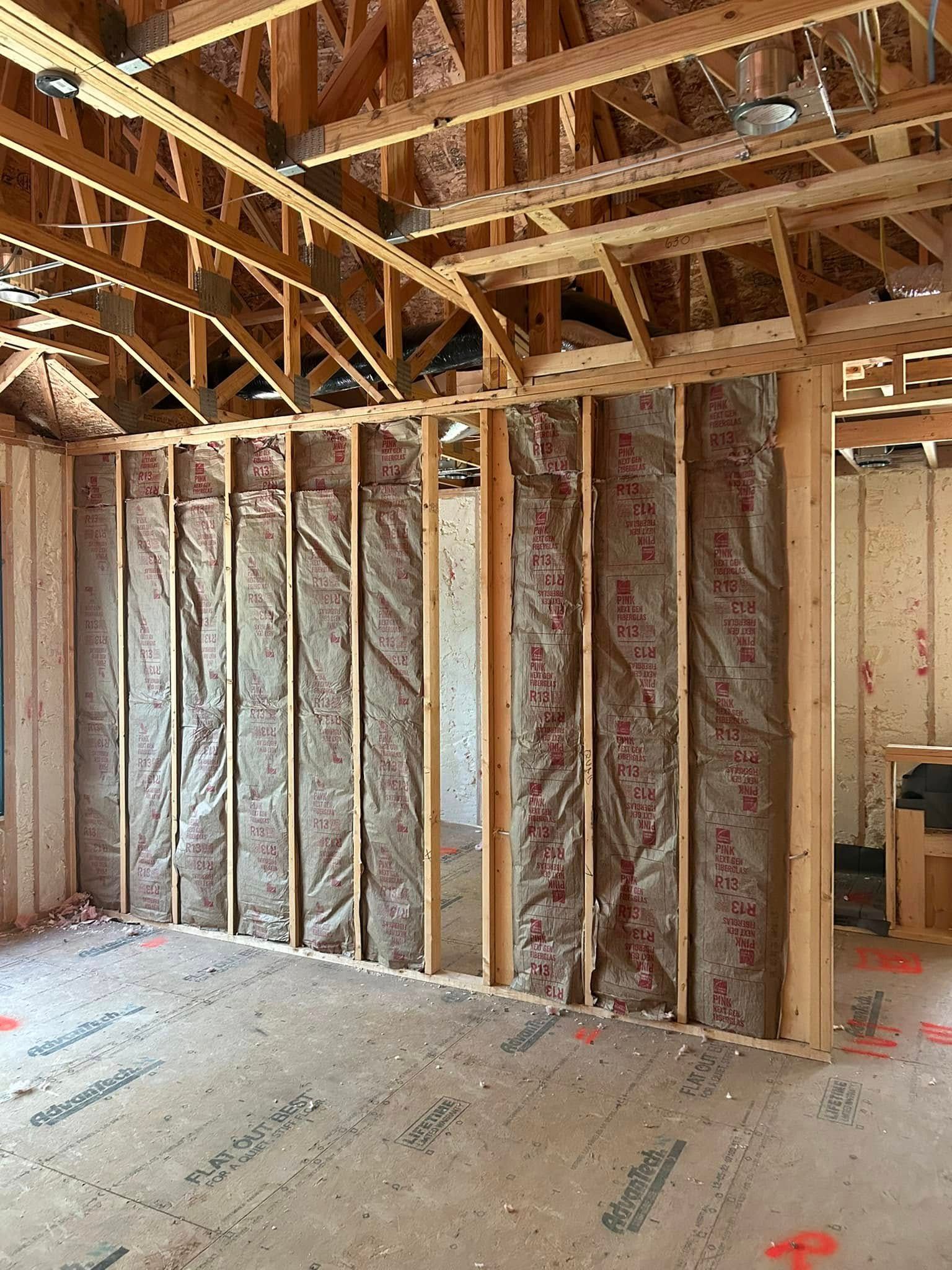 Interior framing of a house under construction, with insulation in the walls and exposed wooden beams.