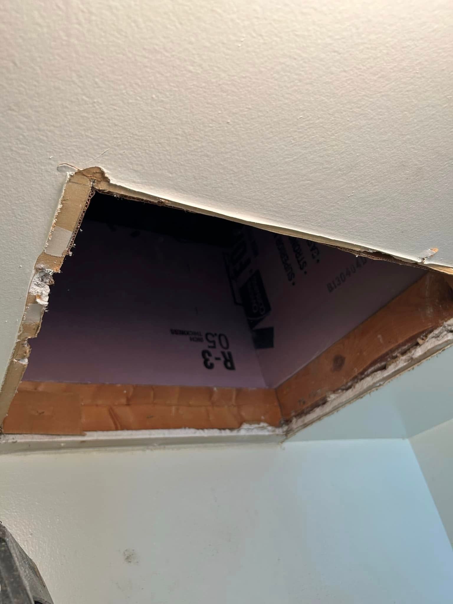 Hole in a white ceiling, revealing pink insulation and brown framing.