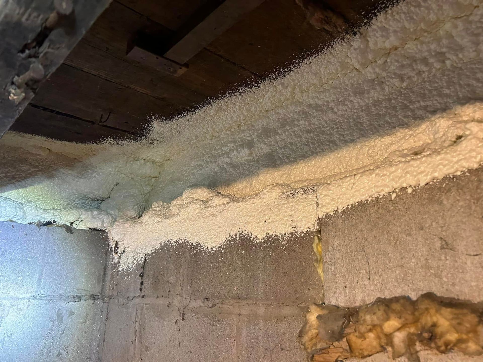 White insulation, resembling foam, is sprayed on the concrete basement ceiling.