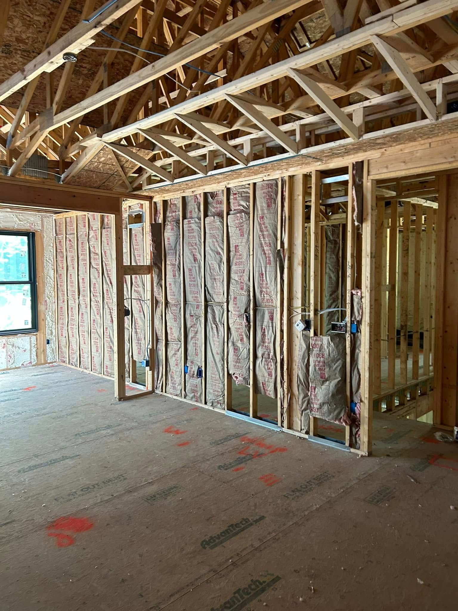 Interior framing of a house under construction; exposed wooden studs, insulation, and electrical wiring.