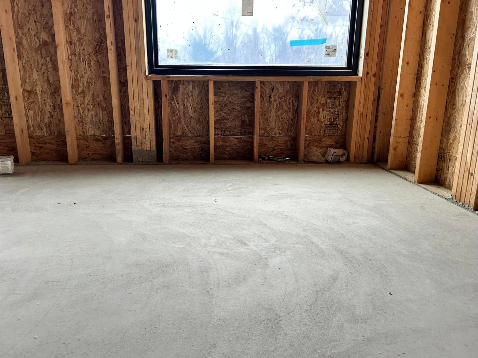 Interior of a room under construction, with wooden studs, concrete floor, and a window.
