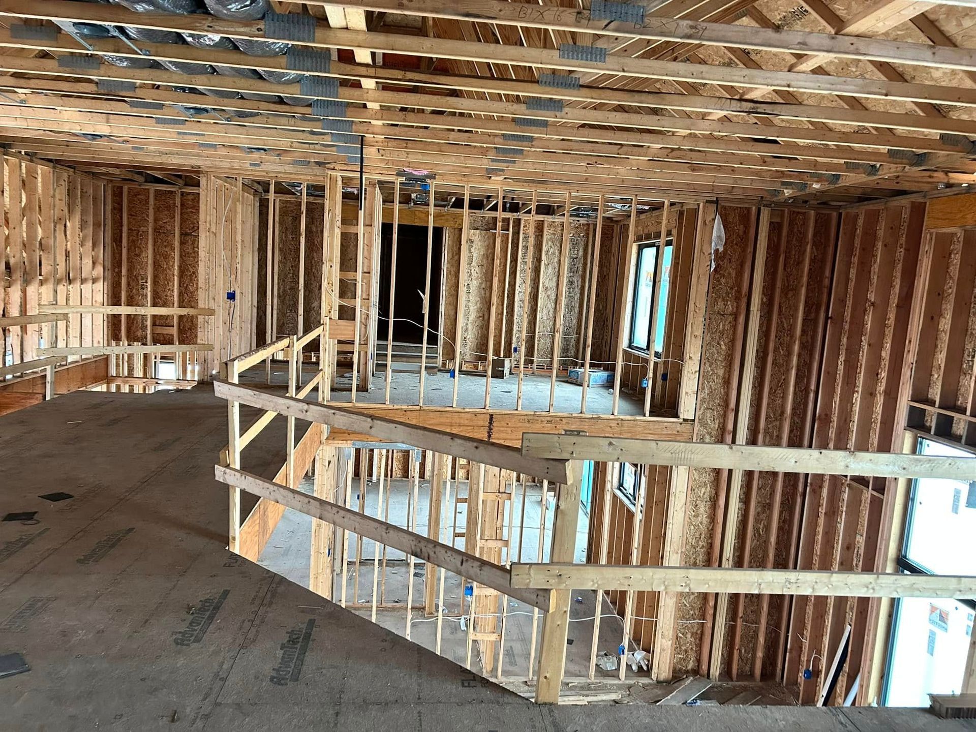 Interior view of a house under construction, showing wooden framing of walls, ceiling, and railings.