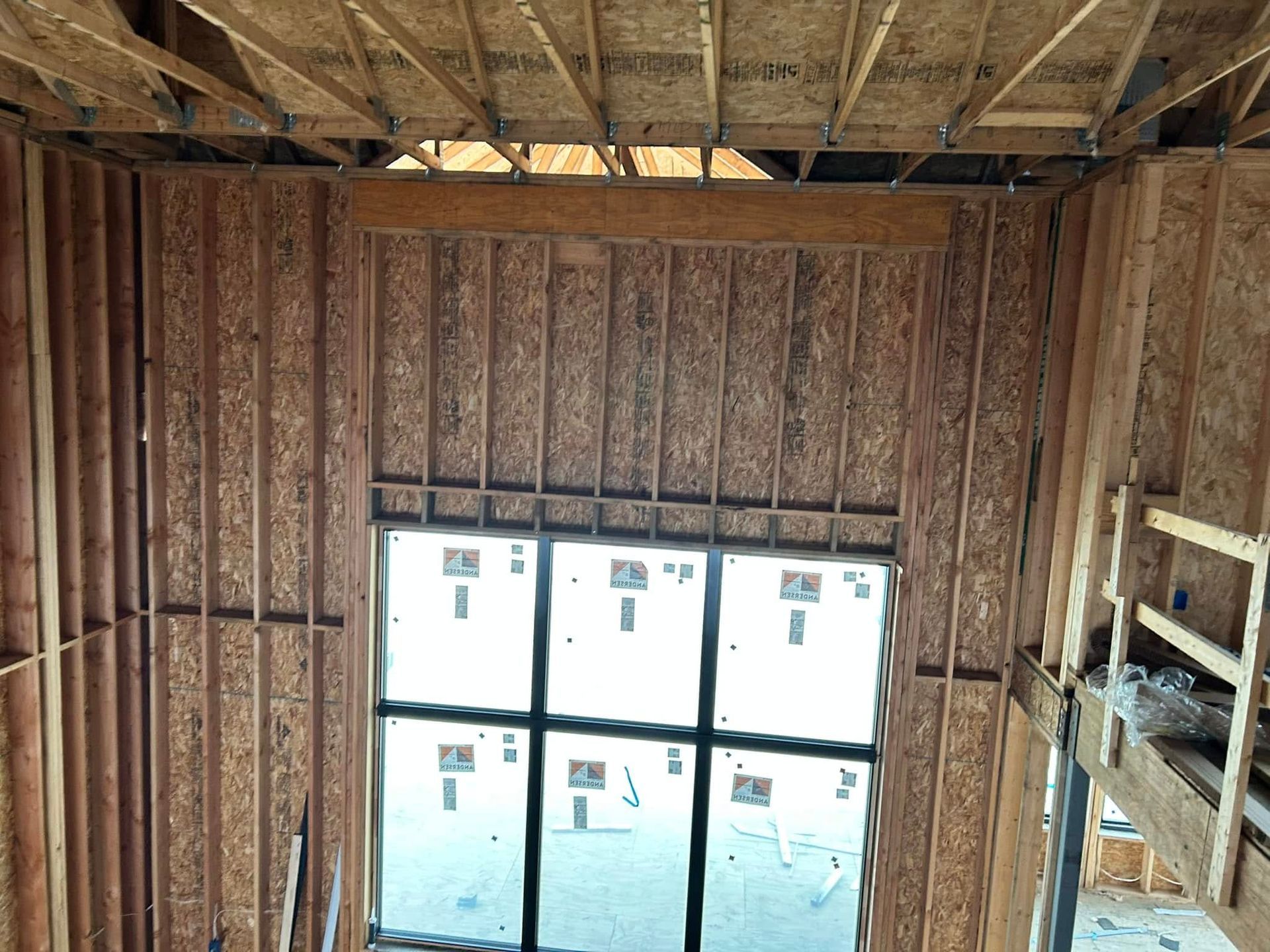 Interior view of a building under construction. Wood framing surrounds a large window looking out to a building.