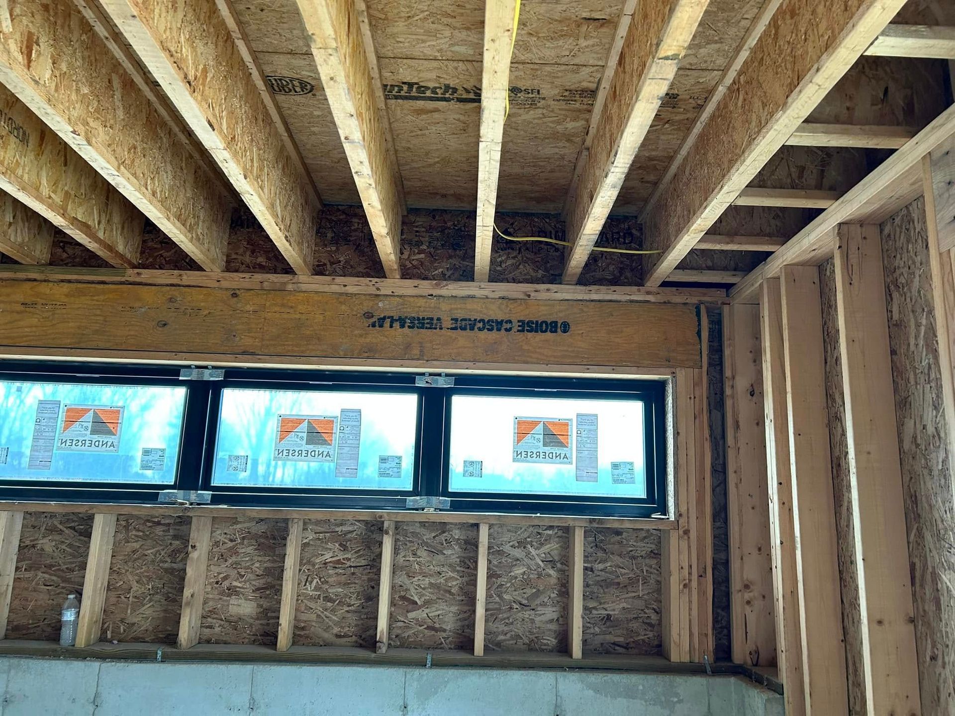 Interior view of a room under construction, showing wooden framework for ceiling, wall, and windows.