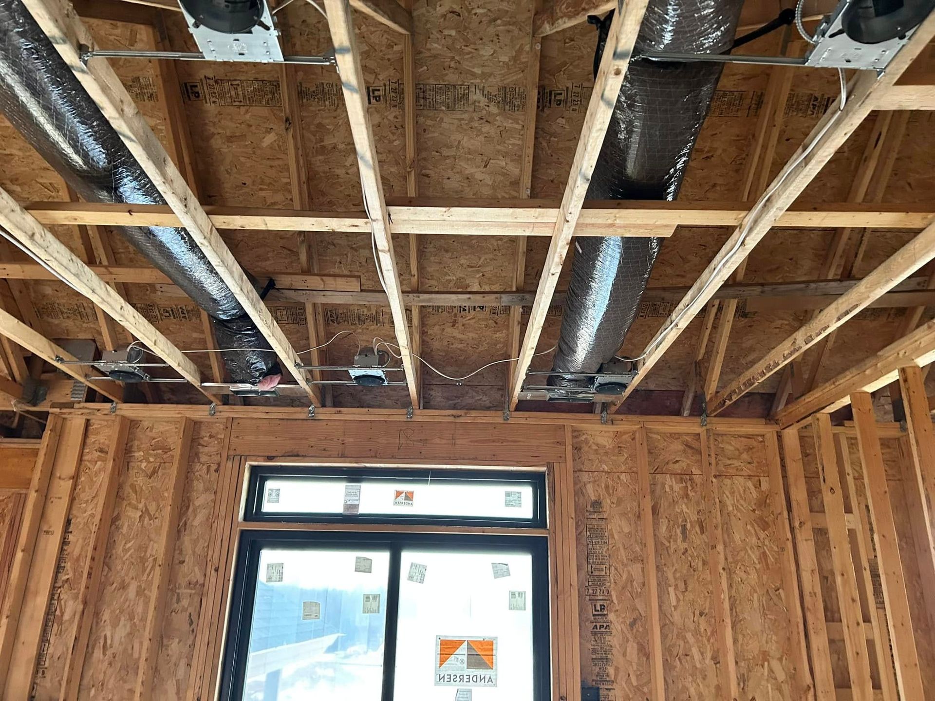 Interior view of a room under construction with exposed wooden framework, air ducts, and a window.