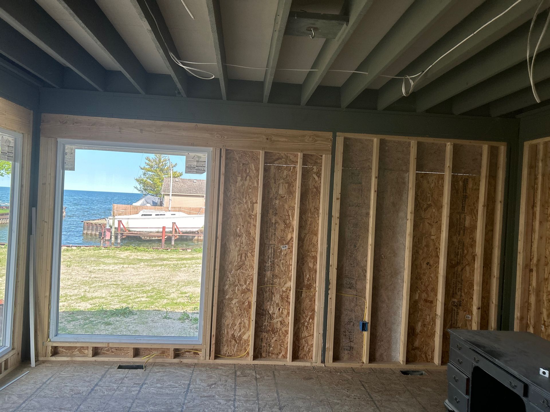 Interior view of a room under construction, with a large window overlooking a lake and partially framed walls.