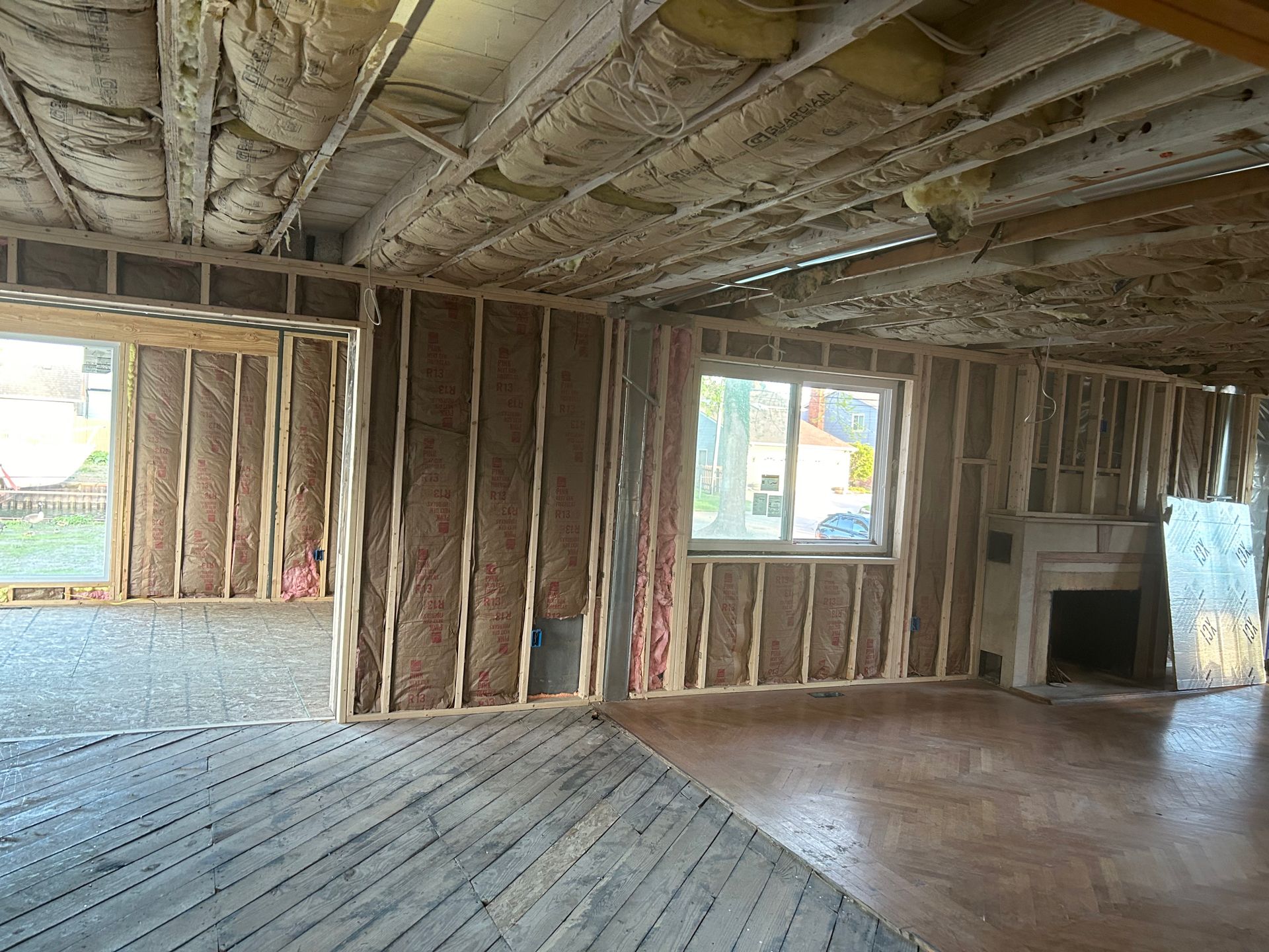 Interior of a room under construction, wooden framework, insulation, window, and a fireplace.