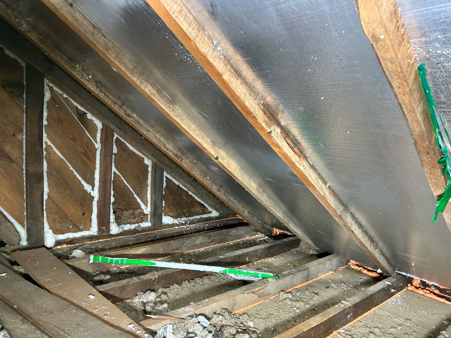 Attic space with wood beams, insulation, and reflective foil. Foam fills triangular spaces.