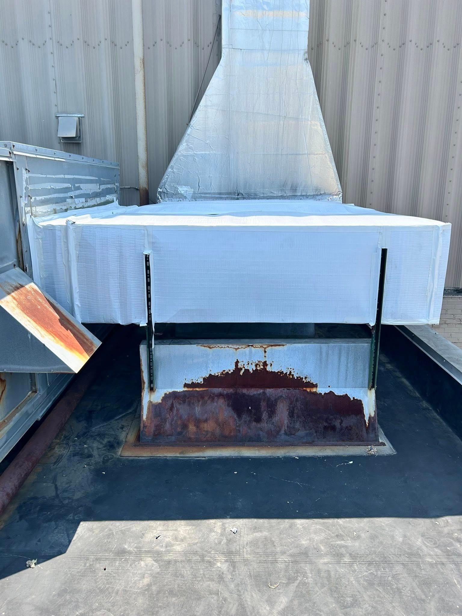 Rooftop ventilation system with a rusty base, surrounded by metal ductwork.