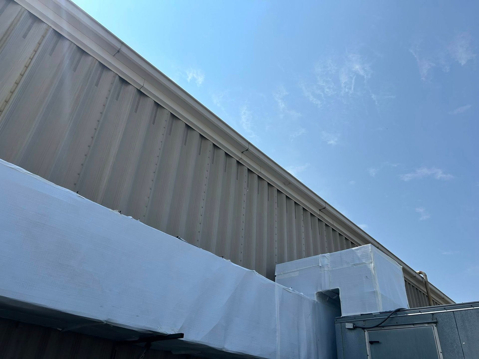 Low-angle view of a corrugated metal building exterior against a bright blue sky.