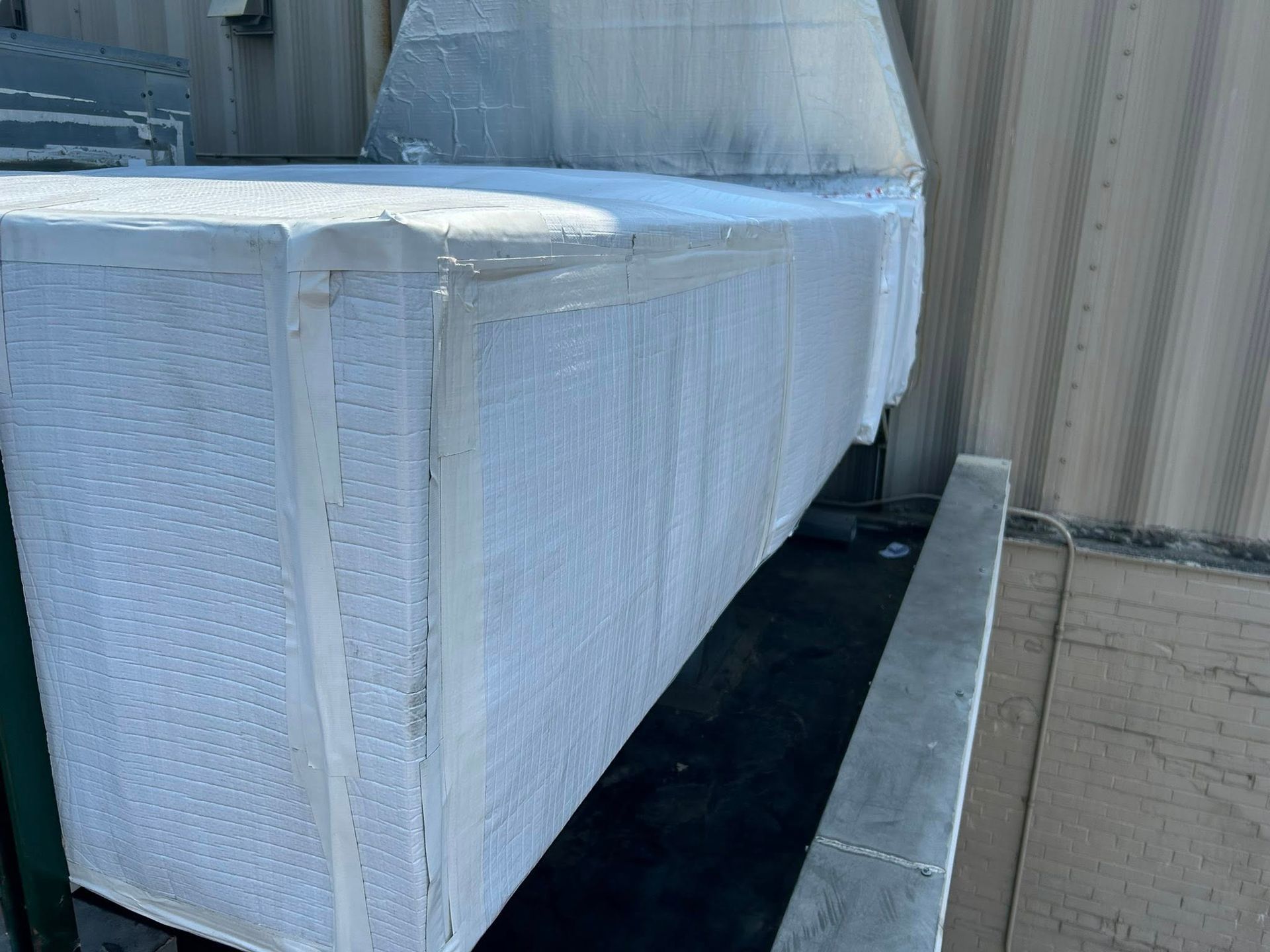White, rectangular, insulated HVAC ductwork on a roof, wrapped in protective covering.