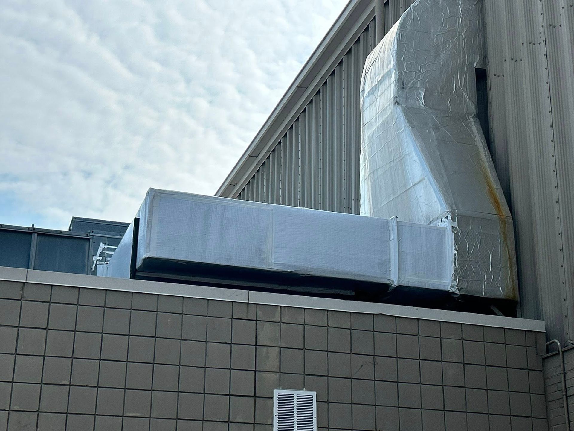 HVAC unit on a building's rooftop, wrapped in protective covering against a cloudy sky.