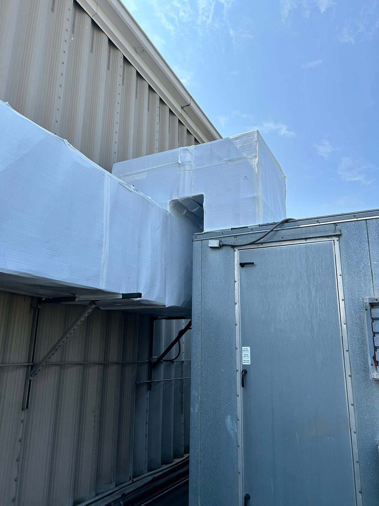 Exterior of a building with metallic HVAC ductwork and an adjacent silver door.