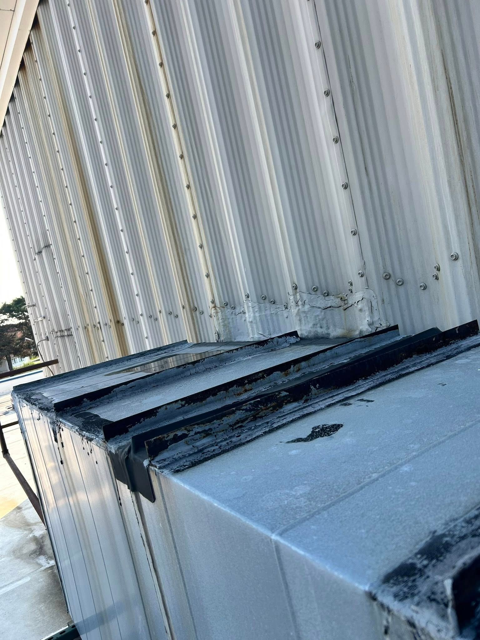 Metal building exterior with corrugated siding, a flat roof, and debris at the base.
