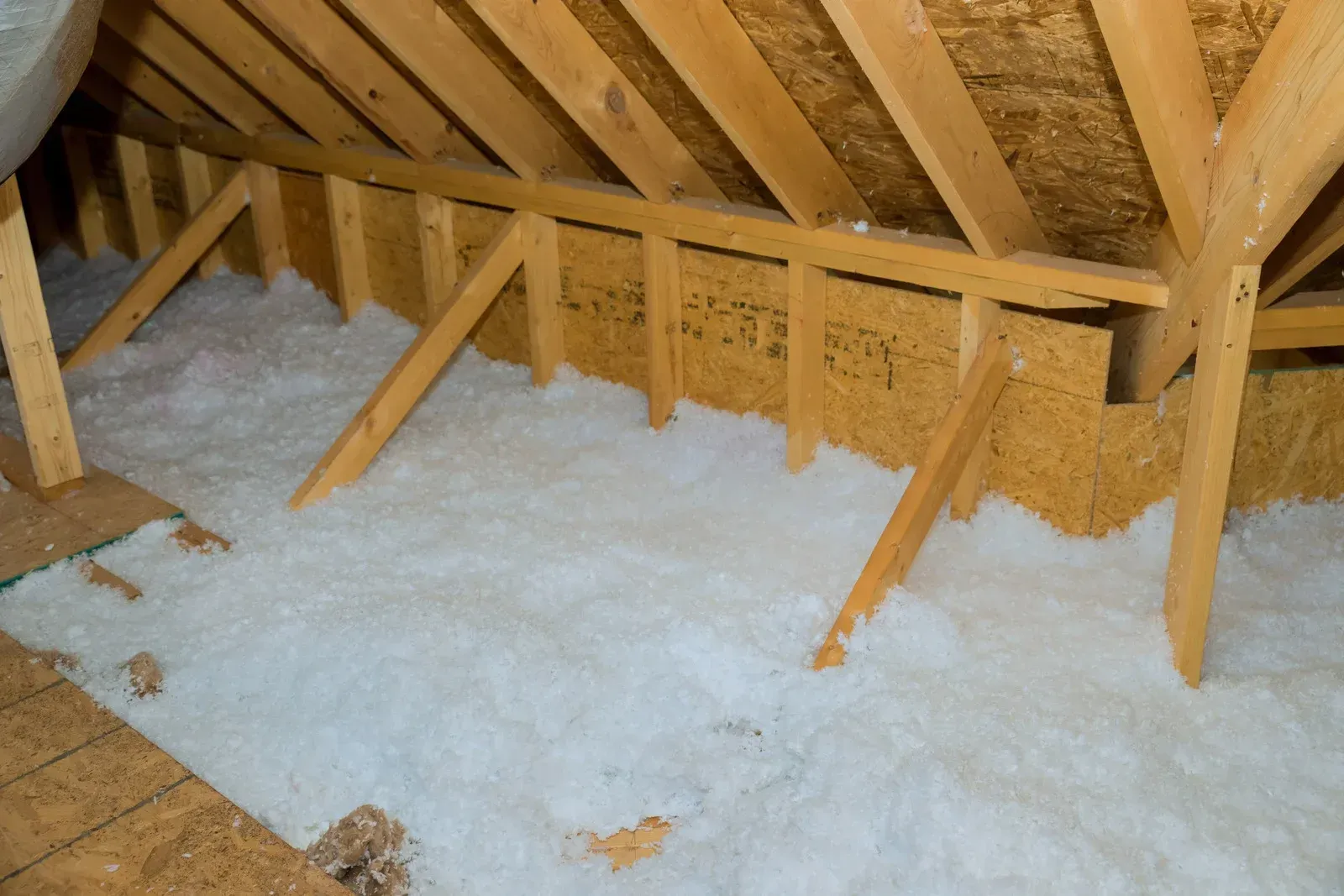 Attic space with wood framing and insulation, lit by a natural light source.