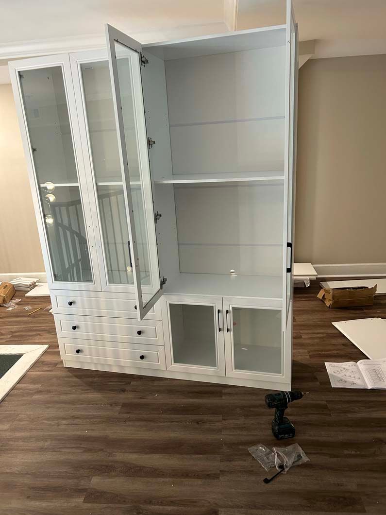 A white cabinet with glass doors is being built in a living room.