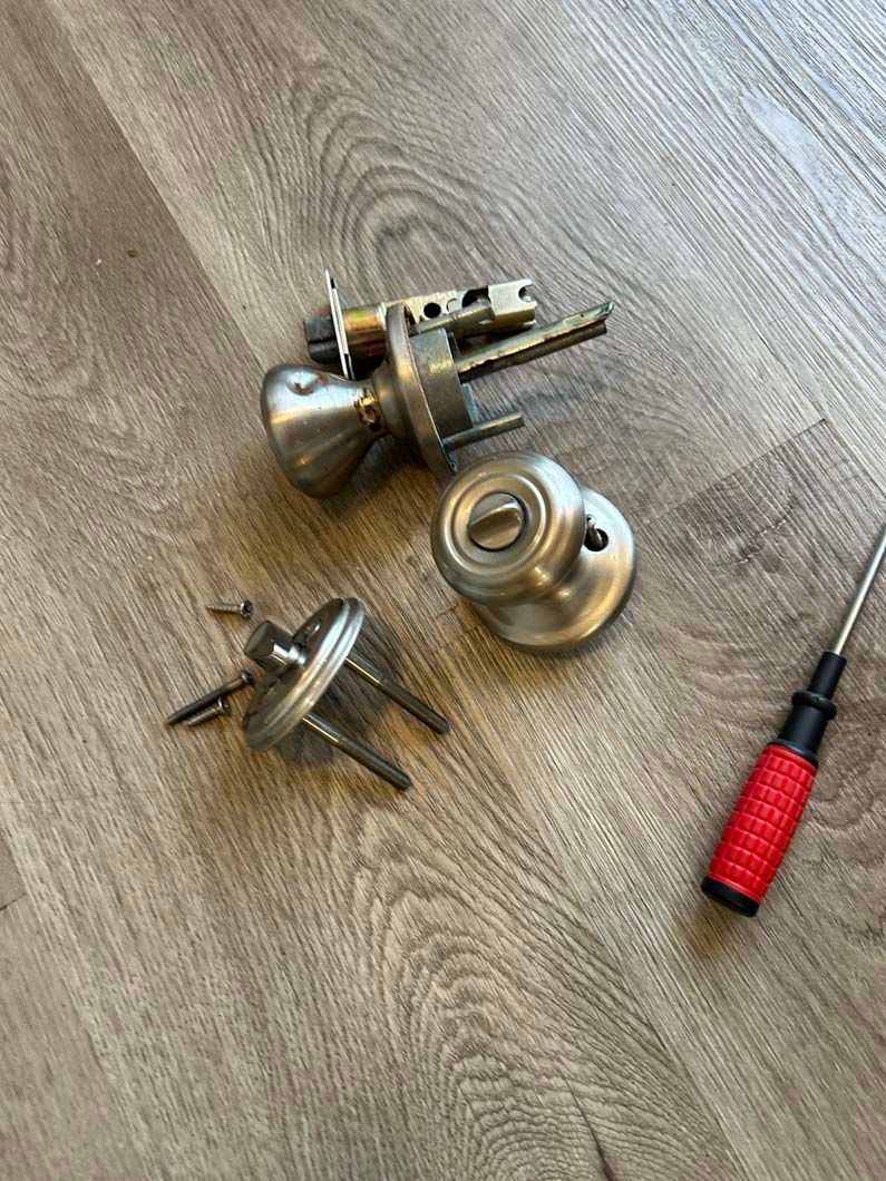 A door knob and keys are laying on a wooden floor next to a screwdriver.