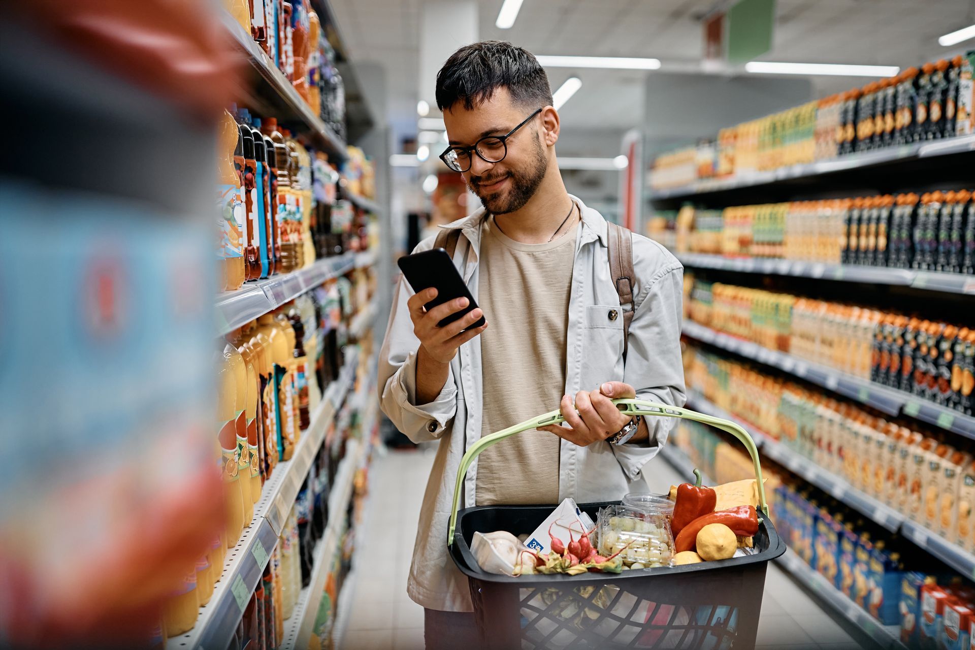 Man with shopping basket grocery shopping and looking at phone