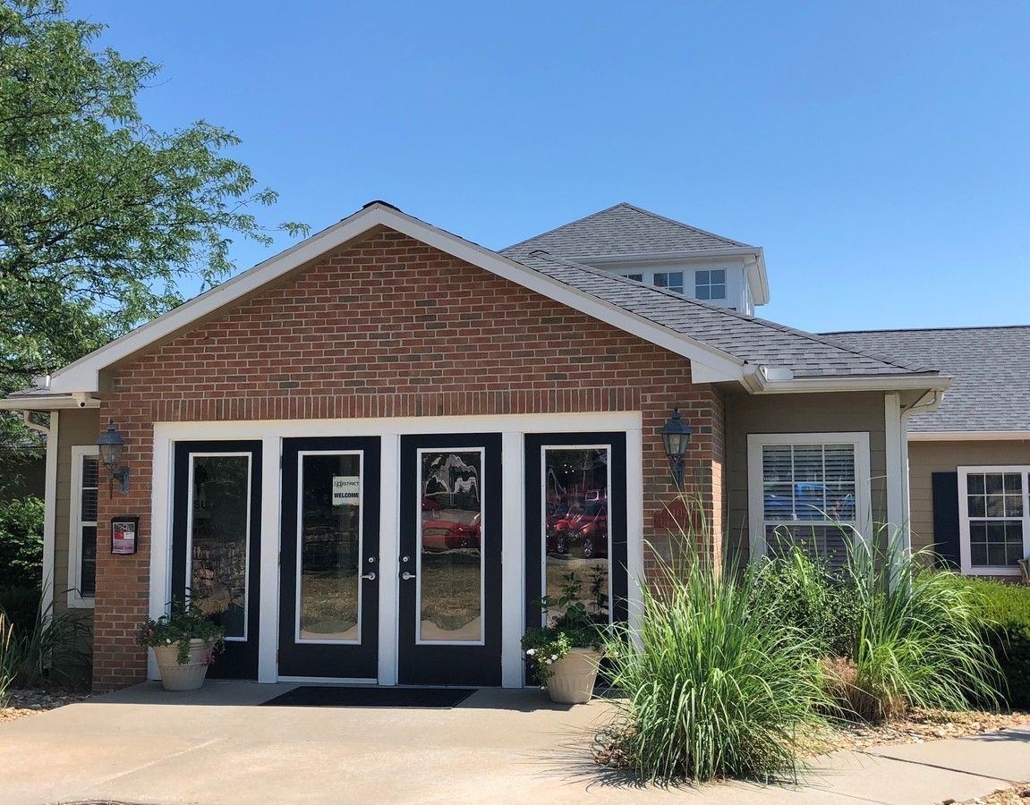 Brick building entrance with glass doors, potted plants, and greenery. Blue sky in the background.