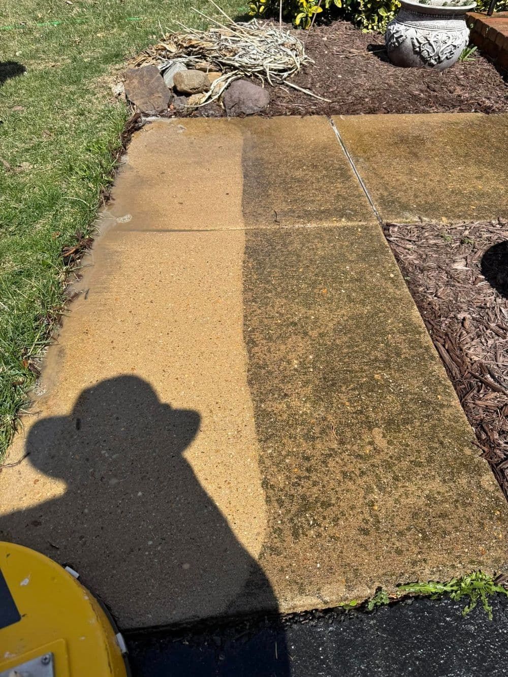 Sidewalk half-cleaned, showing contrast between dirty and pressure-washed concrete. Shadow of person operating the cleaner.