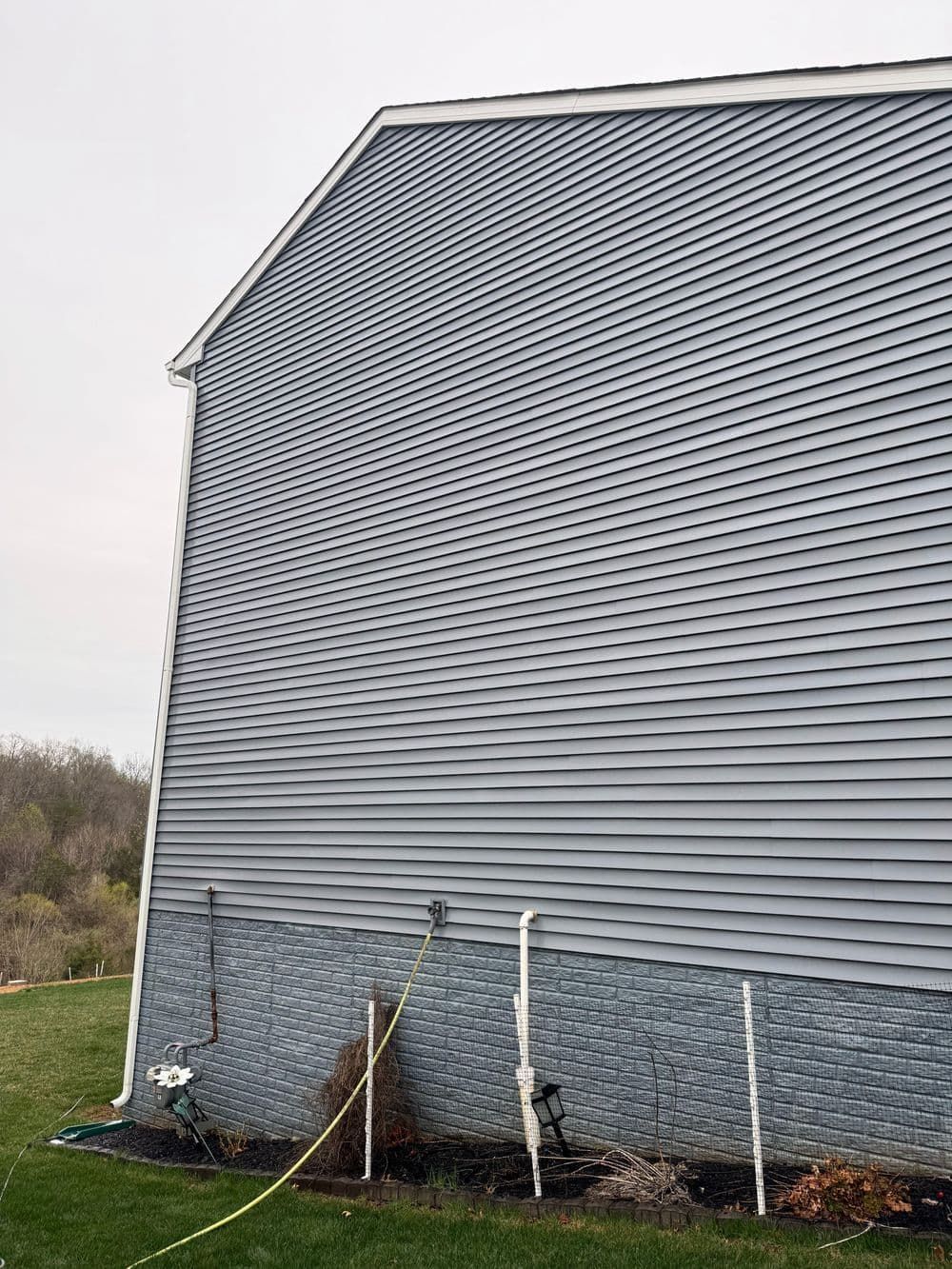 Side of a house with gray siding, beige trim, and a yellow hose in the yard.