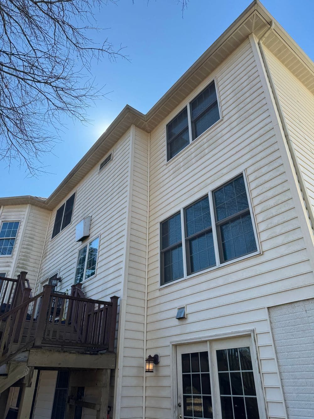 Two-story beige house with several windows, a deck, and a white door. Blue sky in the background.