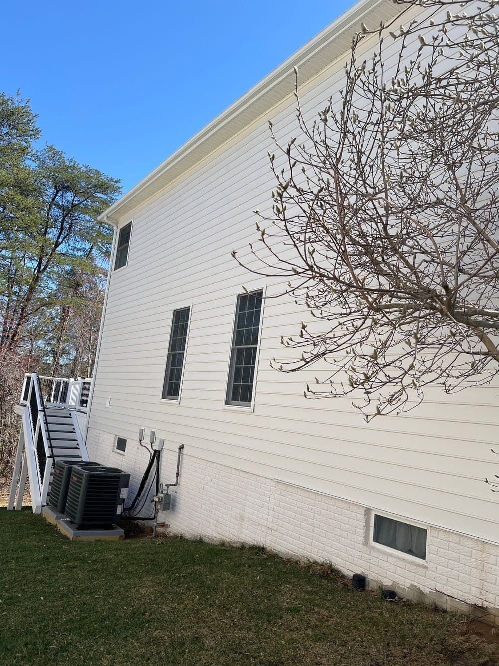 White house exterior with stairs, air conditioning units, and a bare tree on a sunny day.