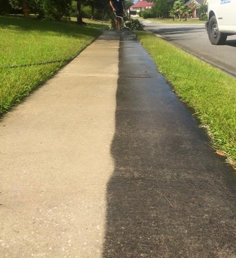 Sidewalk being power washed, showing a clear color difference between clean and dirty concrete.