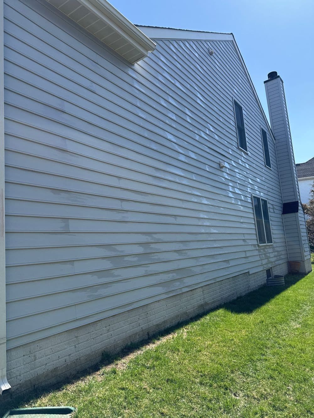 White-sided two-story house with a chimney on a sunny day, viewed from the side with green grass in foreground.