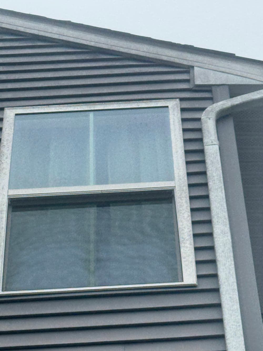 Window with white trim on a gray clapboard house. Gutters are to the right.