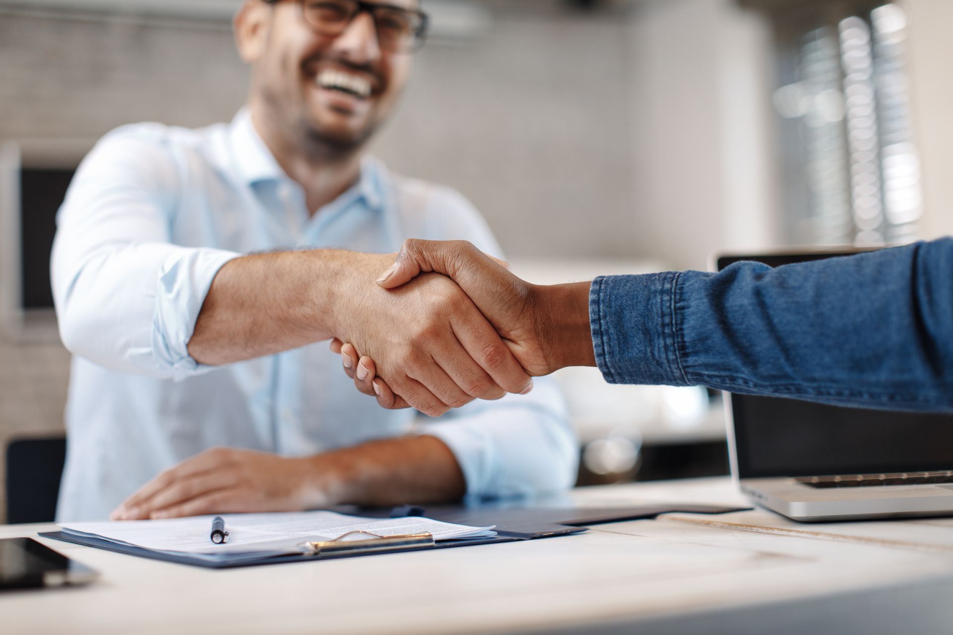 Two men are shaking hands over a table in an office.