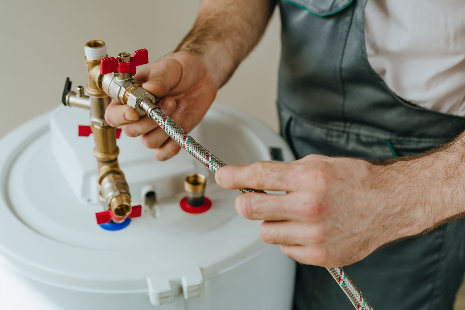 Plumber tightening a brass valve on a white water heater with a wrench and braided hose
