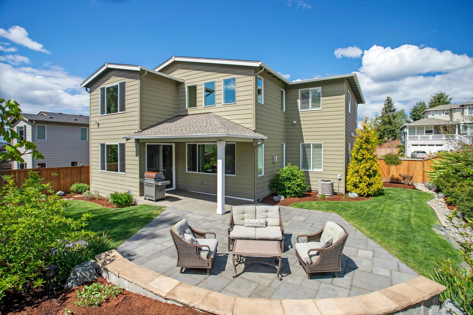 Backyard patio with outdoor chairs and table in front of a two-story house