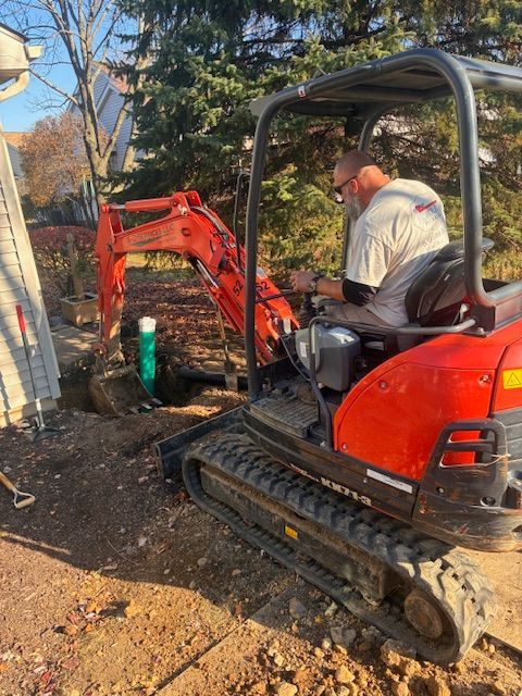 Two workers clearing a drain with a machine on a street, wearing masks and gloves.