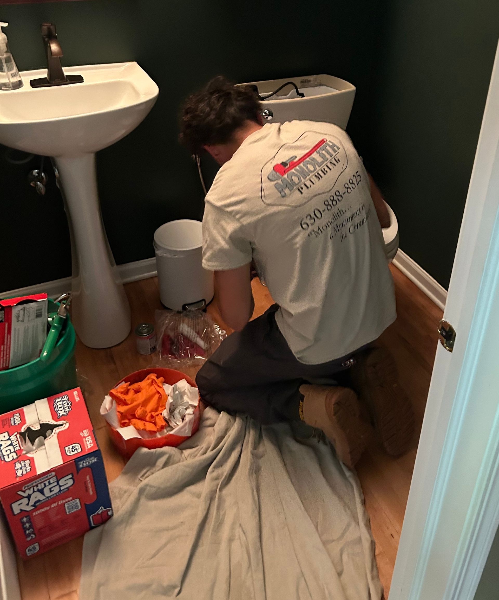 Plumber using wrench to tighten sink pipe in bathroom.