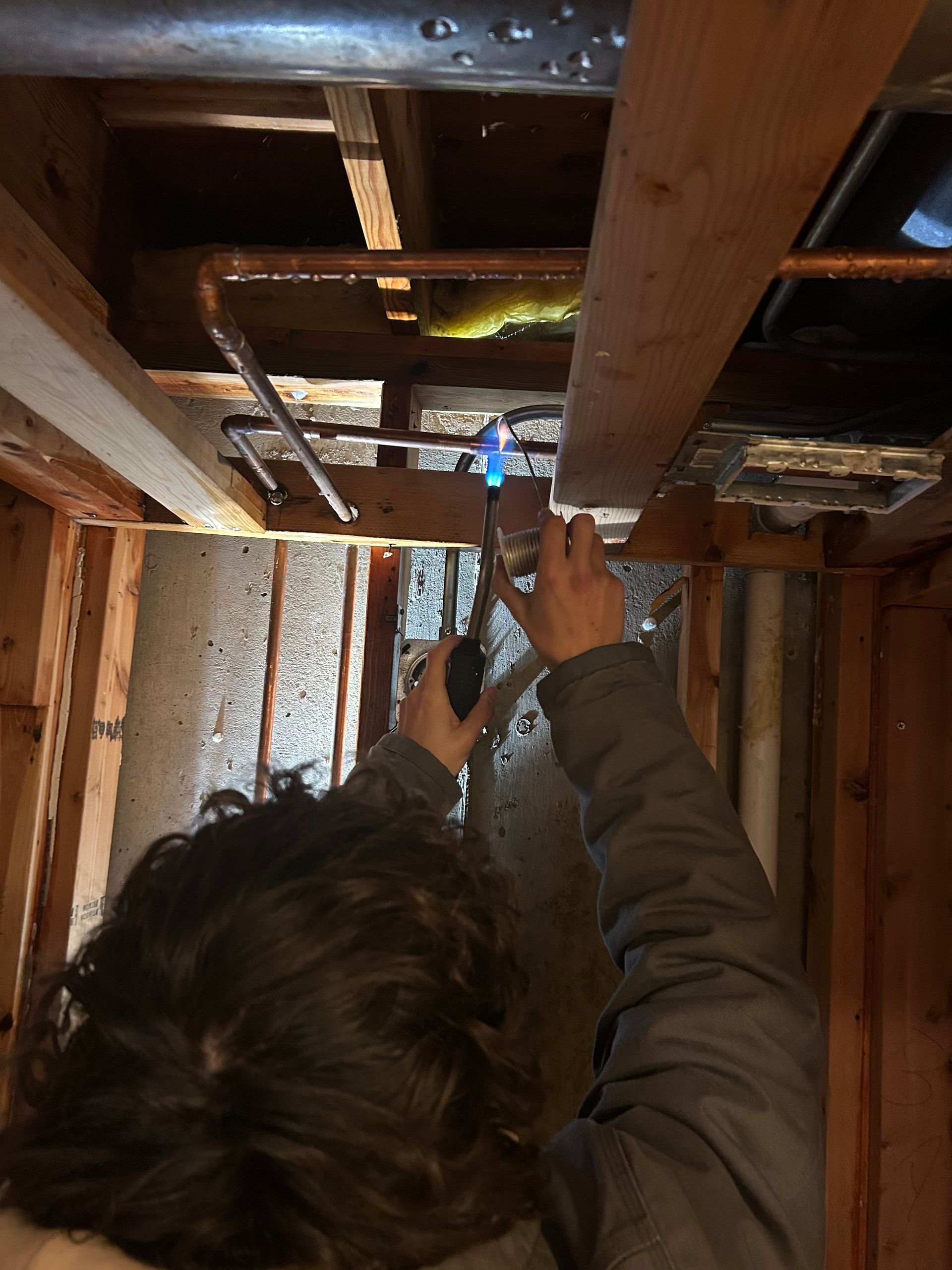 Man in blue shirt working on plumbing under a white sink.