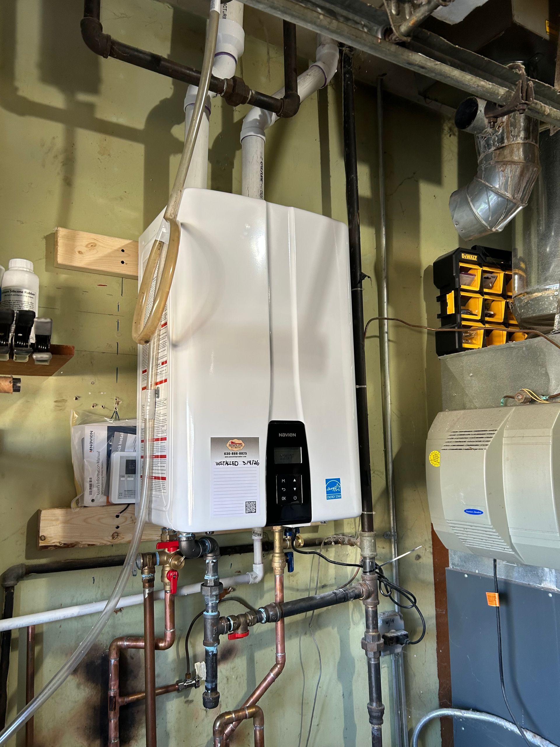 Technician in a cap and overalls inspects a white boiler, taking notes on a clipboard in a utility room.
