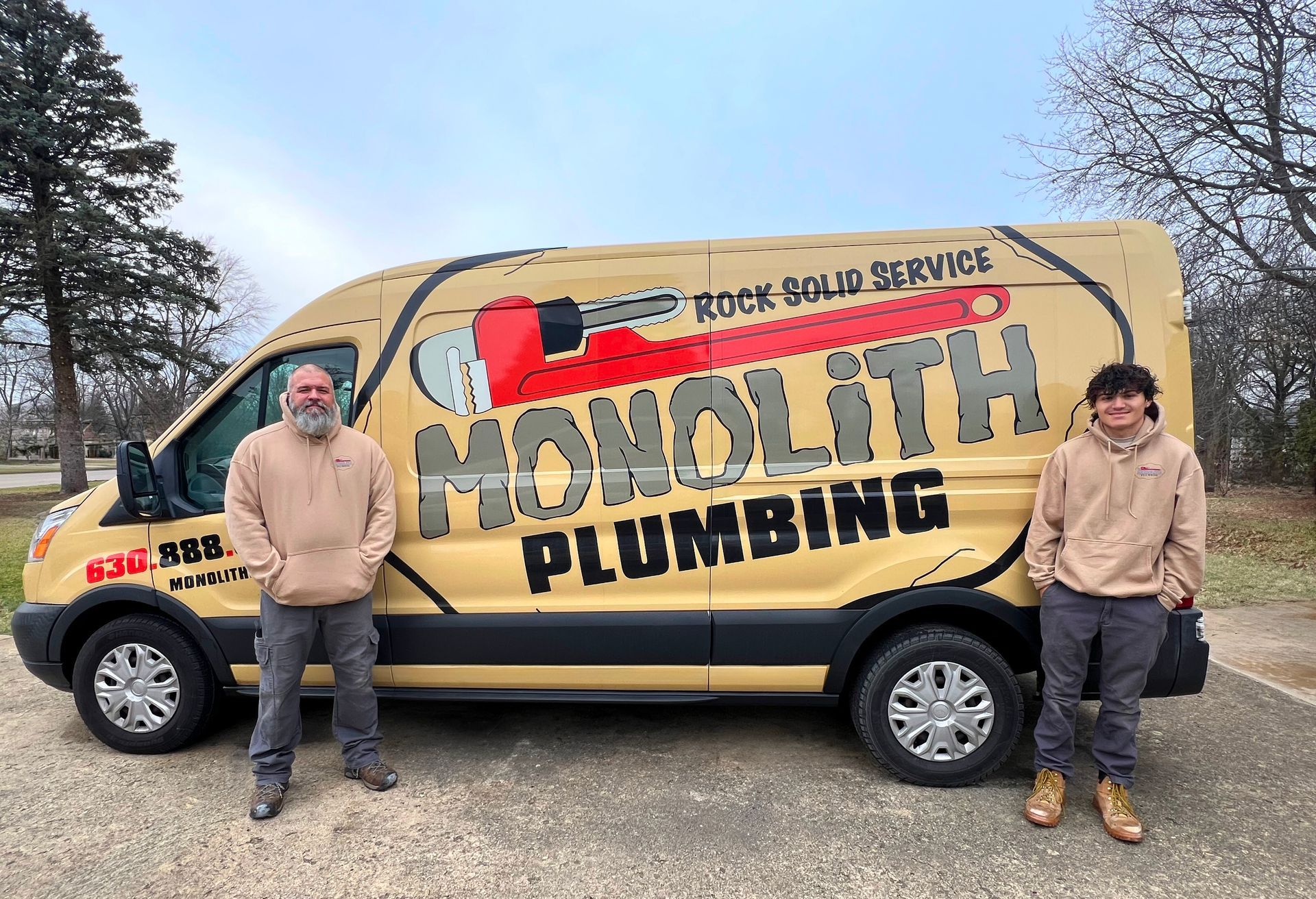 Plumber in safety glasses and gloves using a wrench on pipes, working in a utility area.