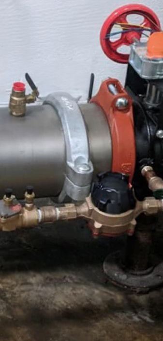 Plumber working on pipes with a wrench and adjusting a valve; setting is indoors.