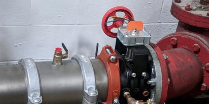 Hand turning a yellow-handled valve on copper pipes in a room with a white wall, likely plumbing repair.